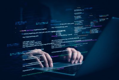 Hands typing on a laptop with programming code overlays, symbolizing VigilantIoE’s expertise in custom software development and agile technology solutions.